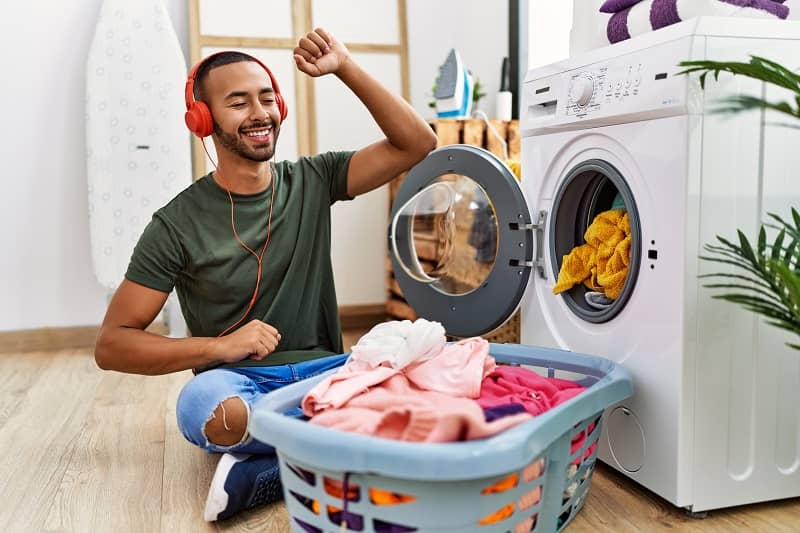 young hispanic man listening to music using washing machine at laundry cm